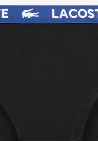 Juodi medvilniniai bokseriai šortai su mėlynu elastiniu juosmeniu, ant kurio baltu užrašu „LACOSTE“ ir logotipu. Lygus tekstūra ir prigludusi forma.