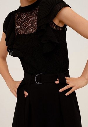 Zwarte top met kantdetails en ruchemouwen, gecombineerd met hoog gewaisted zwarte broeken met een riem met een ronde gesp.