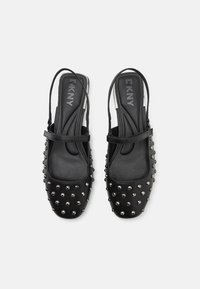 Crne natikače s remenčićem, s glatkom kožnom gornjom površinom ukrašenom metalnim zakovicama, okruglim vrhom i sigurnim remenom oko članaka.