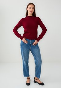 Maglione lavorato a maglia bordeaux con collo alto e maniche lunghe, abbinato a jeans blu a vita alta e svasati e scarpe nere basse.