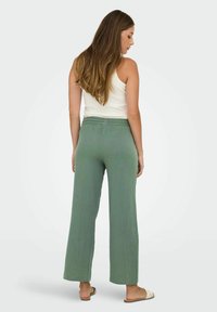 Grønne vide bukser i struktureret stof med elastisk talje, sammen med en hvid tanktop og flade sandaler.