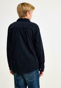 Tmavě modrá kordová košile se solidní texturou a límečkem, s manžetami na knoflík, nošená s světle modrými džíny z denimu se šitými detaily.