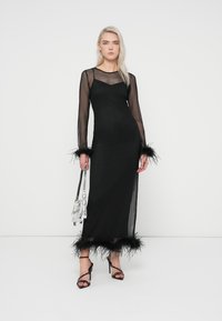 Vestido maxi preto com mangas longas transparentes, detalhes em penas nos punhos e na barra, silhueta ajustada, tecido suave e um sobrepôro transparente.