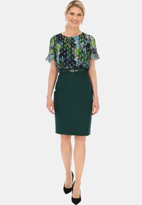 Bluzka z kwiecistym wzorem, z krótkimi, falbankowymi rękawami oraz zieloną spódnicą o kroju ołówkowym, z wąskim paskiem i gładką, dopasowaną fakturą. Czarne szpilki.