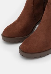 Bruna mocka ankelstövletter med rund tå och texturerad gummisula. Har en siddragkedja och vadderad insida för komfort.