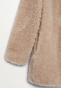 Beige faux shearling frakke med en blød, tekstureret overflade og lange ærmer. Har en let oversized pasform og ingen synlige metaldele.
