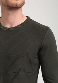 Maglione a maglia verde oliva con un motivo testurizzato e elementi angolari, collo a coste e design aderente.