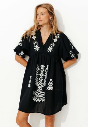 Robe en coton noire avec broderie florale blanche, décolleté en V et manches courtes bouffantes. Silhouette évasée avec un détail de taille froncée.