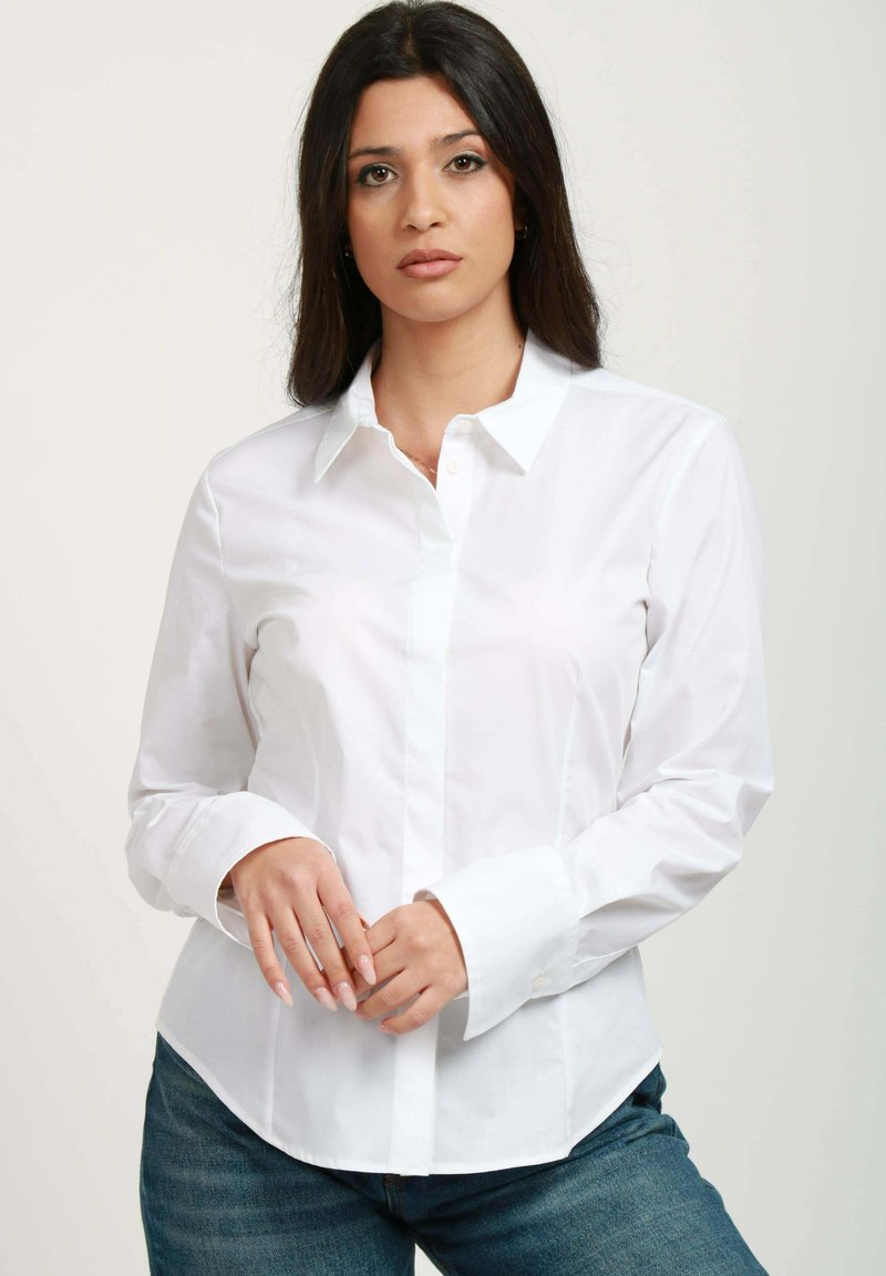 Camicia bianca con bottoni realizzata in tessuto morbido, dotata di colletto classico, maniche lunghe e vestibilità su misura, abbinata a un paio di jeans in denim blu.