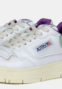 Sneakers bianche in pelle con finitura texture, dotate di accenti viola e verdi, lacci beige e un logo prominente sul lato.