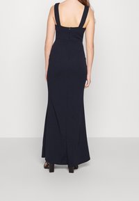 Marinblå, golvlång klänning med breda remmar, figurnära liv och diskret dragkedjeslutning i ryggen. Slät textur, elegant silhuett.