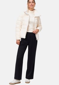 Doudoune beige clair avec un col haut et un rembourrage horizontal. Associée à un pantalon noir taille haute et des baskets blanches.