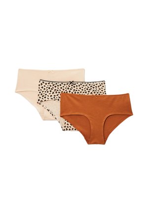 Jeune femme portant un débardeur noir et un sous-vêtement beige à motif léopard, debout devant un fond uni gris clair.