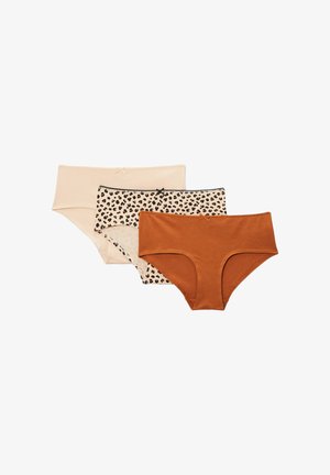 Jeune femme portant un débardeur noir et un sous-vêtement beige à motif léopard, debout devant un fond uni gris clair.