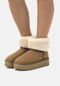 Botas tobilleras marrones con un suave puño de piel de crema, hechas de un material mate, con puntera redondeada y suela gruesa y texturizada.