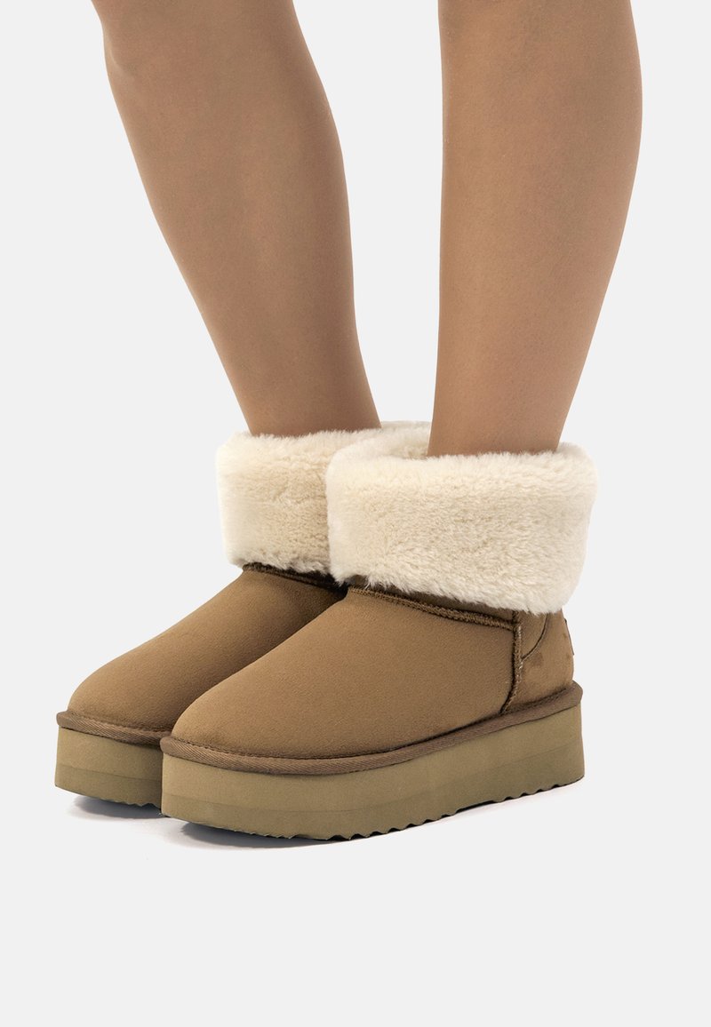 Botas tobilleras marrones con un suave puño de piel de crema, hechas de un material mate, con puntera redondeada y suela gruesa y texturizada.