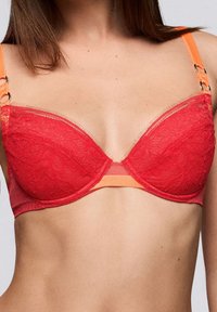 Soutien-gorge en dentelle rouge avec des bretelles accentuées orange, doté d'un design rembourré et d'un bord festonné. Les accessoires remarquables comprennent des anneaux en métal sur les bretelles.