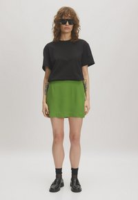 Zwarte T-shirt met korte mouwen gecombineerd met een levendige groene rok. De outfit heeft een gladde textuur met minimale details en zwarte instappers.