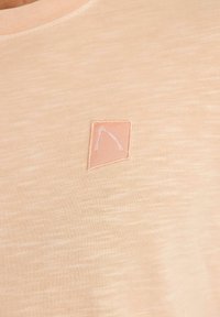 Meruňkové tričko s krátkým rukávem s jemně texturovaným povrchem a malou světle růžovou náprsní kapsičkou s minimalistickým bílým prošívaným designem.