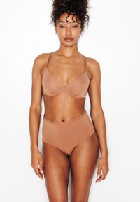 Ensemble de lingerie marron comprenant un soutien-gorge à armatures avec bretelles réglables, associé à une culotte taille haute, tous deux en tissu lisse et extensible.