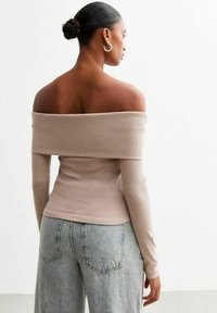 Off-the-shoulder, ribbad topp i ljusbeige, långa ärmar, figurnära design. Kombinerad med högmidjade, löst sittande ljusblå denimjeans.