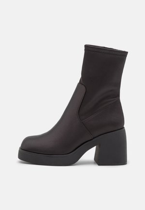 Czarne botki za kostkę wykonane z gładkiego materiału, z masywnym obcasem. Posiadają stylowy, dopasowany cholewkę oraz detale na bocznych szwach, co nadaje im elegancki wygląd.