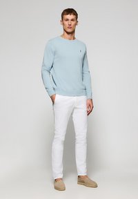 Lichtblauwe gebreide trui met geribde manchetten, gecombineerd met witte slim-fit broek en beige espadrilles. Eenvoudig ontwerp zonder zichtbare patronen.