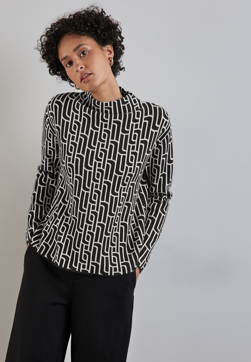 Top largo de manga larga en blanco y negro con un diseño geométrico, textura suave y corte relajado, que presenta un cuello alto.