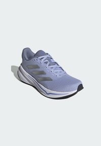 Chaussure de sport violette avec une tige en mesh, un col rembourré, des rayures grises et une semelle texturée. Elle présente un design à lacets et un orteil courbé.