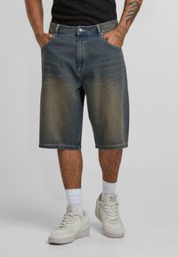 Denim shorts in a faded blue wash, knee-length, with front pockets and a button closure. Paired with white sneakers and ankle-length socks.