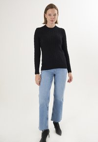 Pull en tricot noir avec un motif côtelé, col rond et manches longues, associé à un jean droit bleu clair et des bottines noires.