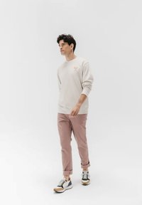 Sudadera gris claro con cuello redondo, logo naranja en el pecho, combinada con pantalones rosa claro remangados en los puños y zapatillas multicolores.