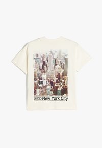 Camiseta de manga corta color crema con una foto del horizonte de Nueva York en la parte posterior, con "NYC" y "Nueva York" impresos debajo.