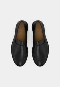 Sorte skinnfrie sko med et elegant design, preget av en glatt tekstur, minimale sømmer og en brun innersåle.