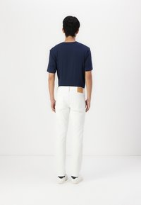 Navy short-sleeve t-shirt paired with white jeans. The jeans have a brown leather patch on the back, showing a slim fit and casual style.