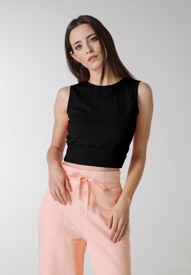 Zwarte crop top met mouwloos ontwerp, ronde halslijn en geribbelde zoom, gecombineerd met lichtroze high-waisted broek met trekkoord.