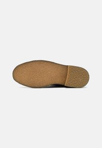 Suela de zapato negra con una superficie texturizada, que presenta una puntera redondeada y un material de goma marrón duradera para agarre y soporte.