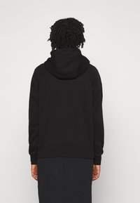 Svart hooded sweatshirt med en strukturerad yta, med en kenguruficka och ribbade ärmslut. Enkel, avslappnad passform utan synliga logotyper.