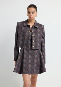 Conjunto de chaqueta corta y vestido en tela estampada con tonos marrones, azules y grises, con botones dorados y una falda acampanada.