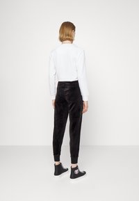 Svarta velourbyxor med ribbade muddkanter och en slät textur, i kombination med en vit långärmad topp, sedd bakifrån. Svarta sneakers ingår.