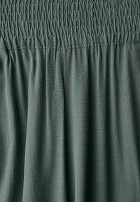 Smocked fabric in muted green, featuring soft, textured draping. Material appears lightweight with gentle sheen and subtle creases.