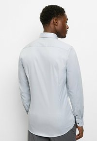 Hellgraues Langarmhemd mit Standardkragen, glatter Oberfläche, Rückenkoller und Knopfmanschetten, mit taillierter Passform und abgerundetem Saum.