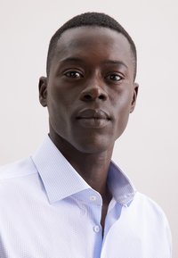 Lichtblauw patroonhemd met knopen en een gestructureerde kraag, versierd met kleine hexagonale ontwerpen, gemaakt van een soepele stof.