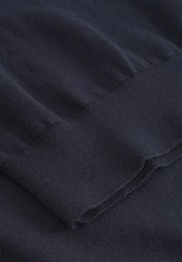 Tatăl de tricotaj de culoare bleumarin închis cu o textură netedă. Imaginea se concentrează pe marginea gulerului rib, evidențiind un model de țesătură curat și uniform.