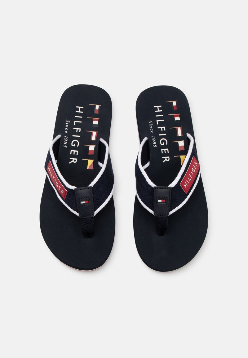 Tongs navy avec une semelle en caoutchouc texturé, dotées d'un contour blanc, de brides en tissu et d'une étiquette de marque rouge avec des détails de logo contrastants.