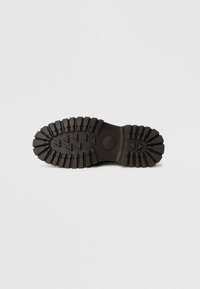 Talpă de cizme negre din cauciuc cu model proeminent al aderenței. Prezintă caneluri adânci pentru tracțiune și un toc neted, rotunjit.