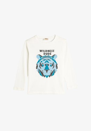 Langærmet hvid t-shirt med et geometrisk blåt og gråt løvegrafik samt teksten "WILDNESS DUDE" over designet.