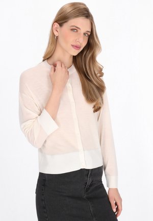 Lichtbeige lichtgewicht cardigan met een ronde halslijn, knoopsluiting en driekwart mouwen, gecombineerd met een zwarte rok. Glad textuur.