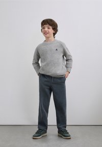 Gray knitted sweater with a round neckline and ribbed cuffs, paired with dark blue corduroy pants and green sneakers with tan soles.
