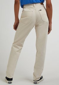 Béžové džíny s vysokým pasem a rovně střiženými nohavicemi, viditelnými zadními kapsami a texturovanou látkou. Vytvořeno v kombinaci s černými teniskami.